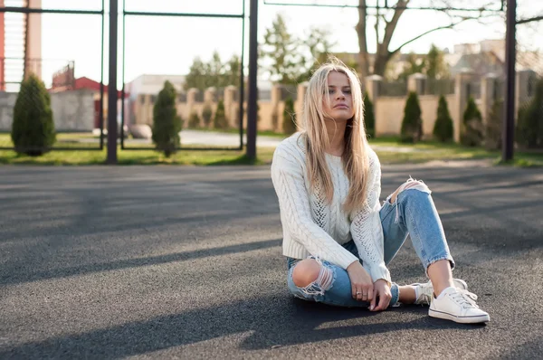 Jonge vrij modieus blonde vrouw gekleed in geripte jeans en witte trui — Stockfoto