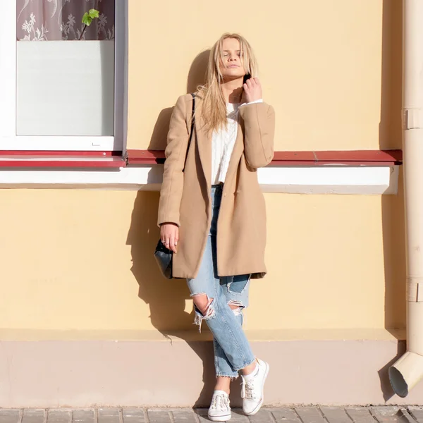 Mulher loira bonita e elegante vestida com jeans rasgados e casaco bege — Fotografia de Stock