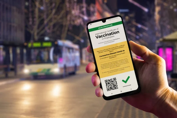 Smartphone arka planda erkek, şehir merkezinde ve belediye otobüsünde COVID-19 için geçerli bir dijital aşı sertifikası gösteriyor. Aşı, hastalık dokunulmazlığı pasaportu, sağlık ve gözetim kavramları