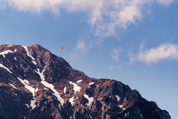 stock image Mountain peak with snow patches and paraglider flying above. Mountaineering, extreme sports and nature concepts.