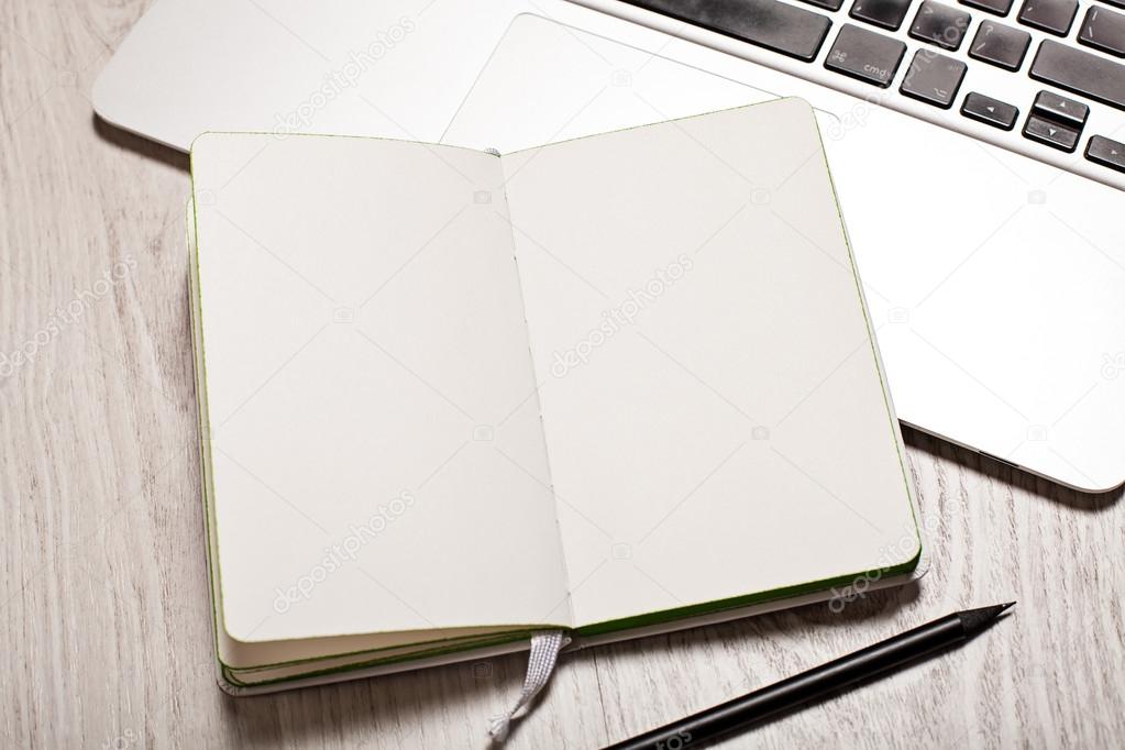 Open notepad with blank pages on white table with laptop