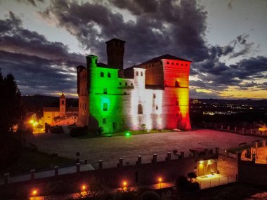 Grinzane Cavour Kalesi 'nin gece görüşü, öncü bulutların önünde İtalyan bayrağıyla aydınlandı.