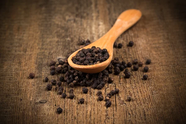 Black pepper on wooden spoon — Stock Photo, Image