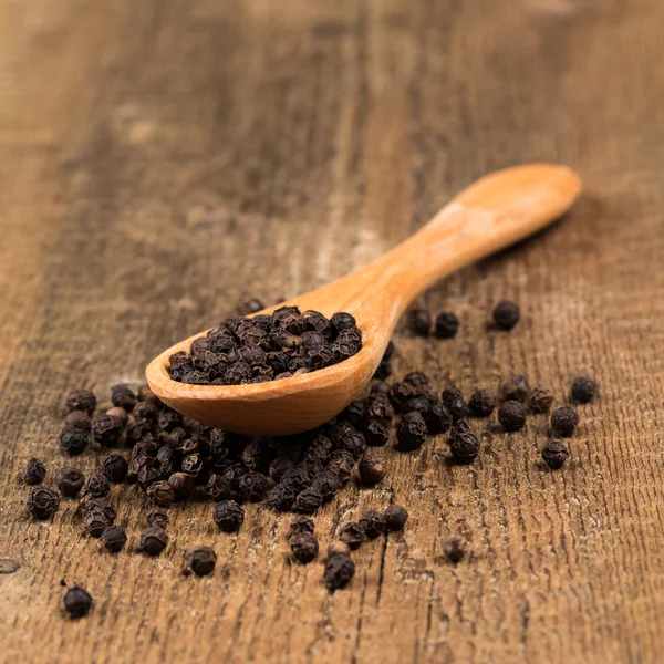 Black pepper on wooden spoon — Stock Photo, Image