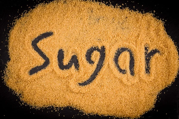 Palavra açúcar escrito em açúcar granulado castanho — Fotografia de Stock