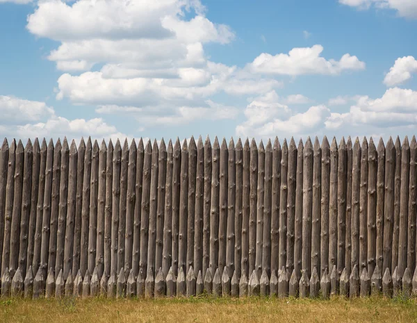 Wooden fence with pointed tips on a background of blue sky with — Stock Photo, Image