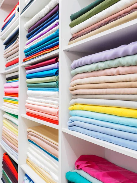 A huge selection of different bright and beautiful fabrics on white shelves in the store. Racks with a large number of fabric samples. large assortment of fabrics in the store\'s warehouse.