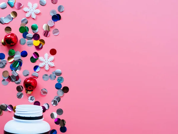 Pills, confetti, Christmas toys on a pink background, flatly, copyspace fall out of the jar. Medical banner concept for new year or Christmas. Ideas for Christmas medical promotions.