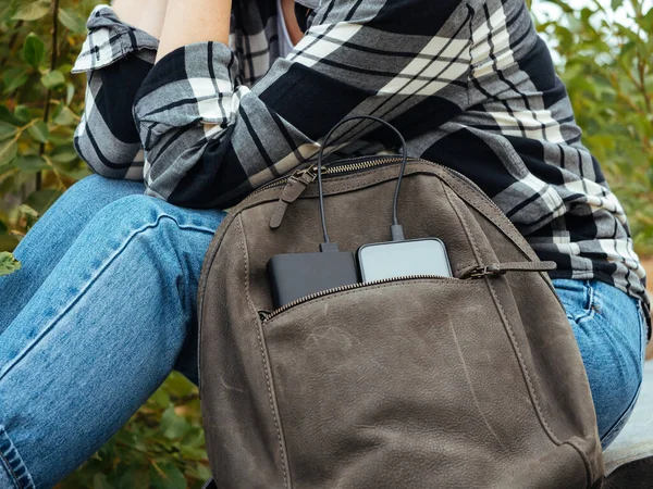 The phone is charged using a power Bank. Use of modern technologies in everyday life. The phone and powerBank are in the tourist\'s leather backpack. Convenient modern gadgets for a comfortable life.