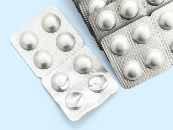 A large stack of tablets in a silver package on a blue background, close-up, mock up. Prevention and treatment of diseases, viruses, coronavirus, flu and colds. The idea of medicine and healthcare.