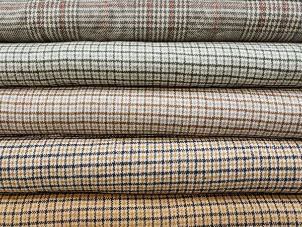 Rolls of different checkered fabrics for sewing coats close-up. Samples of different checkered fabrics are on the shelves in the fabric store. Beautiful and fashionable fabrics for ateliers.
