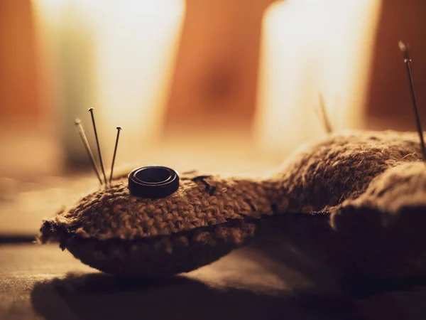 Rag doll voodoo pierced with needles, lying on a wooden table surrounded by burning candles, close-up. The concept of divination, rite, ritual and black magic. Harming people with a voodoo doll.