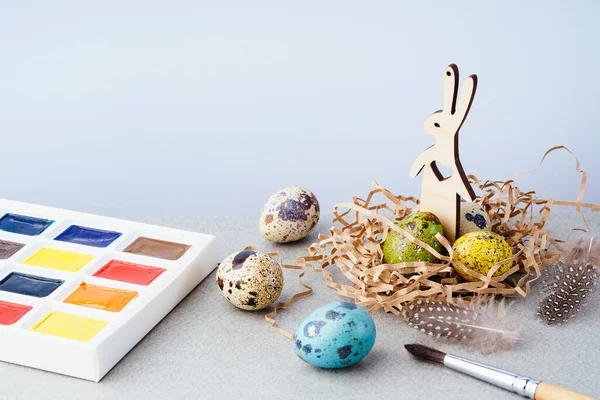 Easter composition with painted eggs in a basket, a rabbit and paints on a gray background. Easter tradition, background. Preparation for the celebration of Easter, a creative concept.