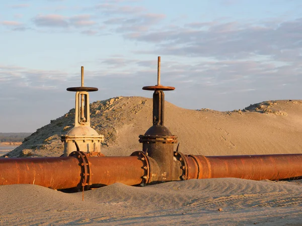 An old rusty oil pipeline in the desert with valves. Pipeline for oil or gas at dawn. Mining of natural resources.