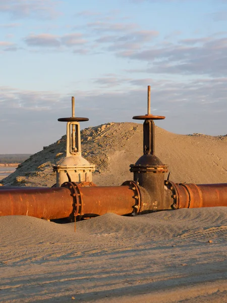 An old rusty oil pipeline in the desert with valves. Pipeline for oil or gas at dawn. Mining of natural resources.