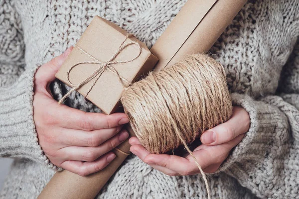 Gifts, craft paper, a coil of rope in women\'s hands, close-up. Handmade gifts concept. Modern trend, natural gift packaging. Holiday background.