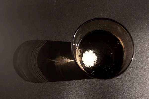 Effervescent tablet dissolving in a glass of water at black background