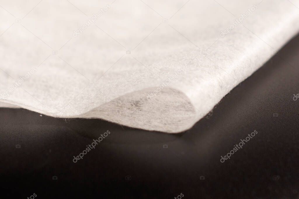 Disposable synthetic non- woven cleaning cloths in a roll, on a black background.