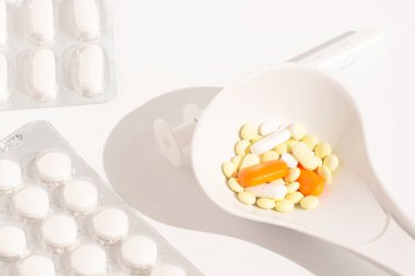 Beyaz kaşıkta çeşitli ilaç hapları, haplar ve kapsüller.