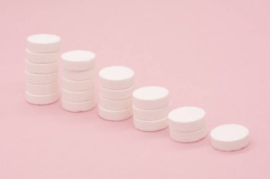 Pembe arka planda bir yığın hap. Kümelenmiş beyaz haplardan oluşan büyüme grafiği - büyüyen pazar ve artan beyaz hap talebi ve onun yerine geçen.