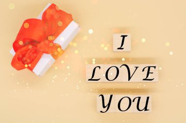 Kırmızı saten kurdeleli el işi hediye kutusu ve tahta bloklara yazılmış seni sevdiğim metin. Sevgililer günün kutlu olsun, doğum günün kutlu olsun, 8 Mart. Tatil konsepti