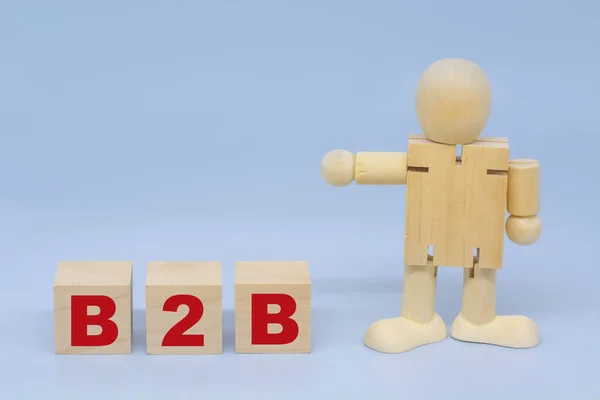 A wooden figure of a man points to an inscription B2B on wooden cubes. Business and corporate concepts