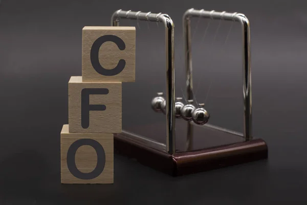 text CFO - Chief Financial Officer on vertical row of wooden blocks and Newton\'s cradle . Business concept.