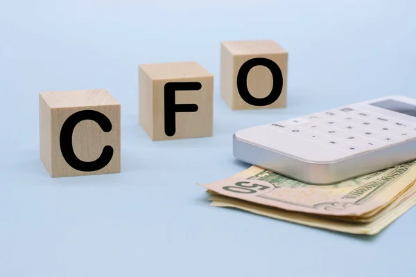 text CFO - Chief Financial Officer of wooden blocks CFO and white calculator. Chief Financial Officer acronym on wooden cubes on blue backround. Business concept.