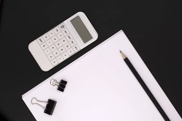 white calculator on black background, paper and pencils. Office desk. Business concept