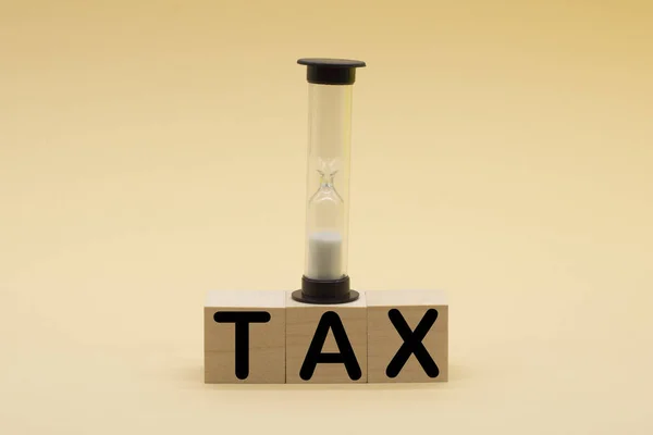 Parola tassa sui cubi di legno e clessidra. Concetto aziendale e fiscale. Pagare le tasse — Foto Stock
