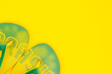 Sarı arka planda sarı-yeşil parmak arası terlikler. Yaz ve eğlence konsepti