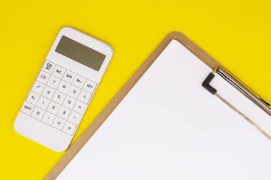 Sarı arka planda beyaz hesap makinesi ve kağıt yazıyorum. İş konsepti
