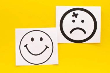 Mutlu yüz ve sarı arka planda üzgün yüz. Pozitif düşünce konsepti.