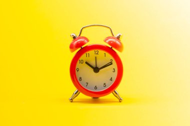 Sarı arkaplanda kırmızı yuvarlak analog alarm saati var. Saat 10: 10.