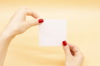 Modaya uygun kırmızı manikürlü kadın eli kartvizit tutuyor. Yaz bahar tırnağı tasarımı.