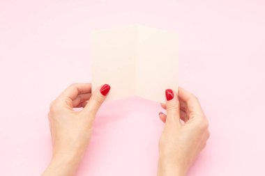 Kadınların elleri, pembe arkaplanın üzerine mektup yazmak için boş broşür tutuyor.