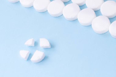 Yuvarlak beyaz tıbbi haplar düzenlenmiş ve bir tanesi mavi arka planda dört parçaya bölünmüş. Hap bölme.