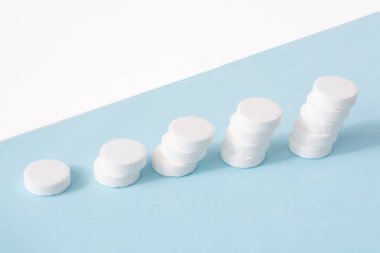 Mavi arka planda bir yığın hap. Kümelenmiş beyaz haplardan oluşan büyüme grafiği - büyüyen pazar ve artan beyaz hap talebi