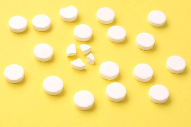 Yuvarlak beyaz tıbbi haplar sıralanmış ve biri sarı arka planda dört parçaya bölünmüş. Hap bölme.