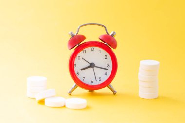 Haplar, tabletler ve sarı arka planda kırmızı alarm saati. Asgari tarzda tıbbi ve sağlık konsepti.