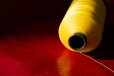 Kırmızı deri üzerinde sarı iplik makarası. Dikiş ipliği