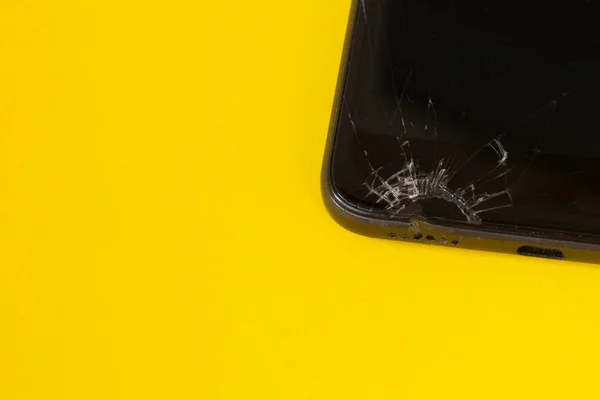broken black mobile phone, screen crack on yellow background