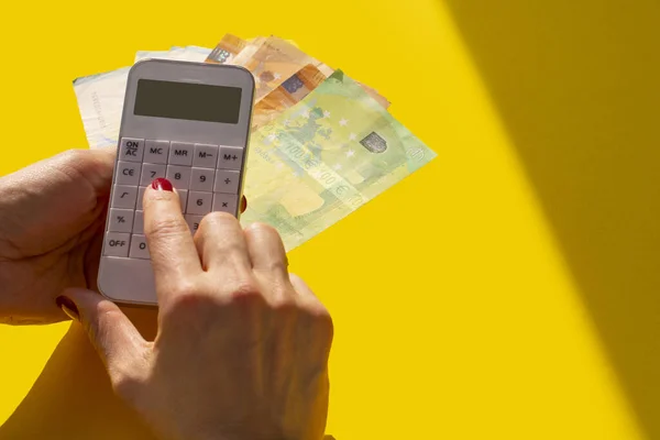 a white calculator in a woman\'s hand and euro banknotes on a yellow background. Planning concept