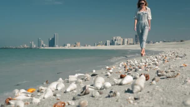 Nierozpoznana młoda dziewczyna w okularach przeciwsłonecznych spaceruje wzdłuż plaży na tle pięknych muszli i piasku. Dubaj Emiraty Arabskie Beach. — Wideo stockowe