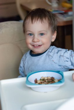 Mutfakta fındık tabağının önünde duran mutlu beyaz bir çocuğun dikey portresi..