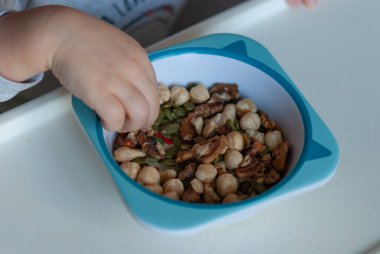 Bebek elleriyle çocuk tabağından çiğ fındık yiyor..