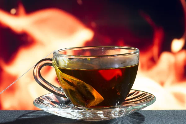 Taza de vidrio de té negro sobre un fondo de fuego — Foto de Stock