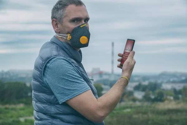 Man wearing a real anti-pollution, anti-smog and viruses face mask and checking current air pollution with smart phone app