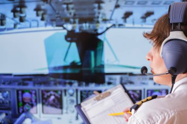 Üniformalı, apoletli ve kulaklıklı güzel bir kadın pilot, uçaktaki not defterine yazıyor.
