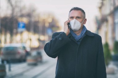 Antivirüs maskeli bir adam telefonda konuşuyor. Şehir caddesinde yürüyor.